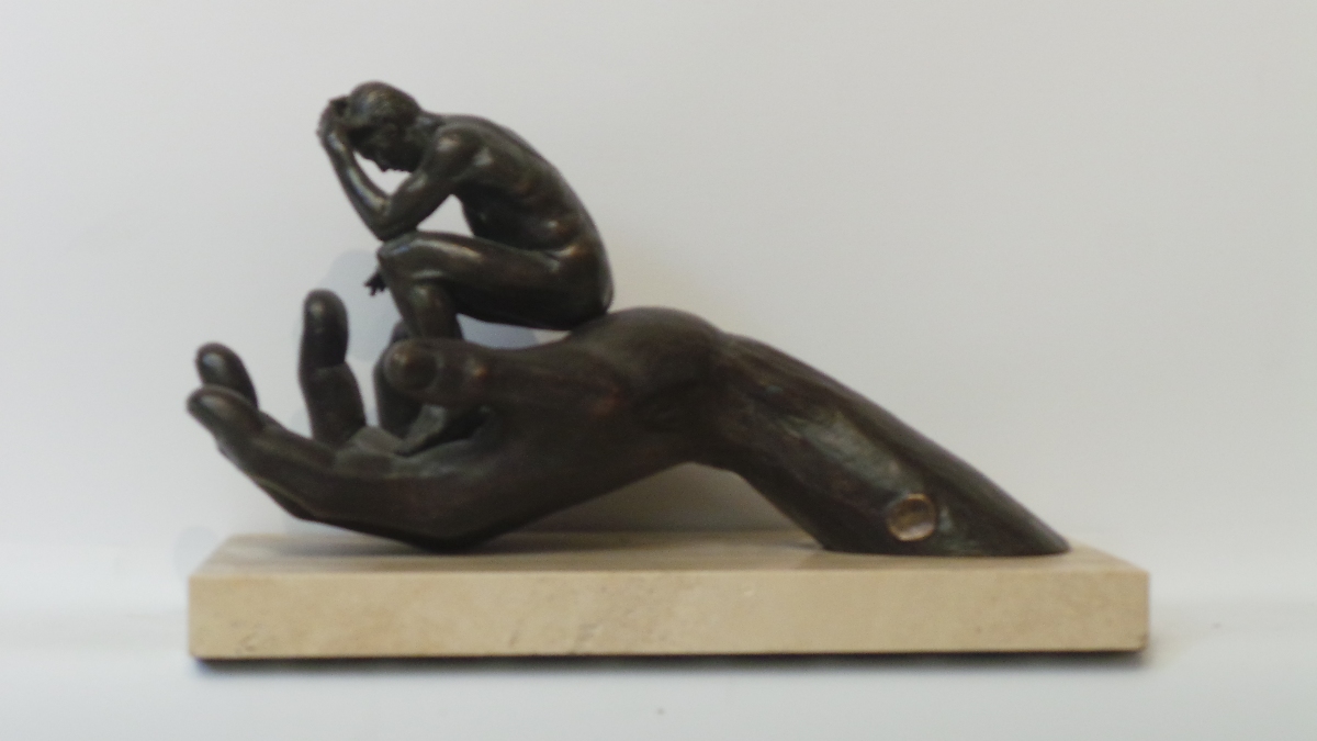 A bronze model of an upturned hand holding a seated man resembling Rodin`s ``The Thinker``