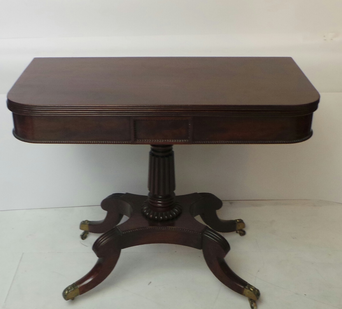 A George V mahogany card table the foldover top raised on reeded turned column descending onto
