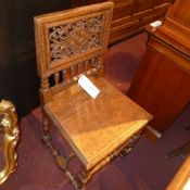 An early C20th oak hall chair with pierced and carved back and spindles above solid seat raised on