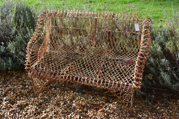 A white painted iron wirework garden seat, early 20th century, with outscrolled back and arms above