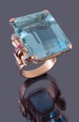 A 1940s `Retro` aquamarine, ruby and diamond ring, the large step cut aquamarine weighing 71.96