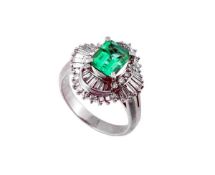 An emerald and diamond cluster ring, the central step cut emerald claw set above a surround of
