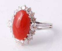 A coral and diamond cluster ring, the central oval cabochon coral panel (corallium rubrum) within a