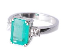 An emerald and diamond ring, the rectangular shaped emerald in a four claw setting, between two