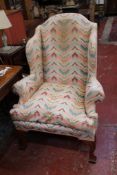 An 18th Century style upholstered wing armchair with arched back and out swept arms on shaped