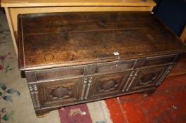 An antique Flemish oak coffer with a plank lid and triple panel front, carved with recessed fielded