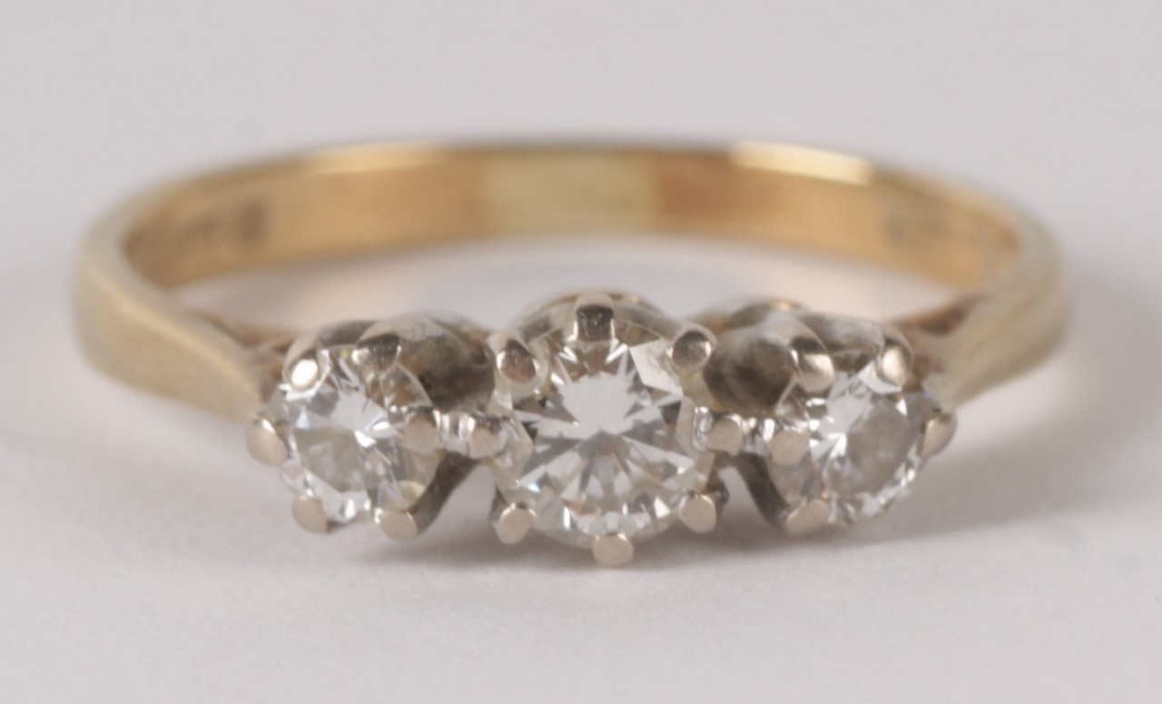 An 18 carat gold three stone diamond ring, the graduated brilliant cut diamonds in claw settings,