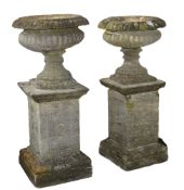 Two similar carved limestone garden urns on plinths, 19th century  Two similar carved limestone