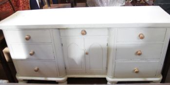 A cream painted dresser base with central drawer and cupboard with arched panelled doors flanked
