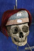A human skull; together with a Chinese embroidered `skull` cap, hung with hair, (2). There is no