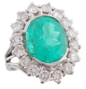 An emerald and diamond cluster ring, the oval shaped emerald in a semi...  An emerald and diamond