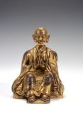 A Tibetan gilded figure of a monk, 18th century, seated on a throne with hands folded in prayer in