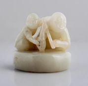 A white jade carving depicting two figures on top of what appears to be a drum, the boy seems to be