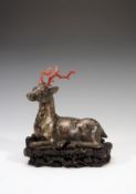 A bronze model of a recumbent deer, its legs tucked beneath it its head raised and alert, the metal