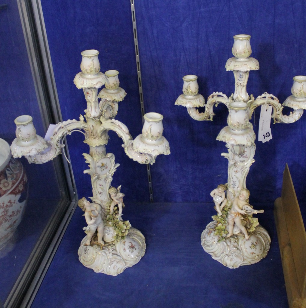 A pair of three branch porcelain candelabra decorated with putti to the base; 46.5cm high