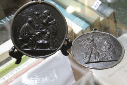 A pair of cast iron circular plaques decorated with classical figures, both with pewter trims, 12cm