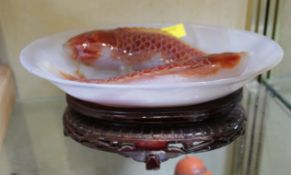 A Chinese glass oval dish decorated with moulded fish and held on a hardwood stand; 24cm wide x 17.