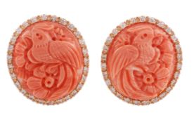 A pair of coral and diamond ear clips, the oval coral carved with a bird amongst foliage, within a s