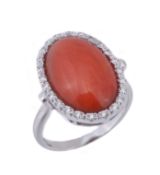 A coral and diamond ring, the oval cabochon coral (Corallium Rubrum) within a surround of