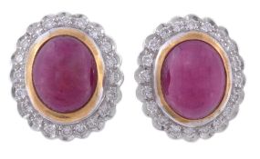 A pair of ruby and diamond ear clips, the central oval cabochon ruby in a collet setting, within a s