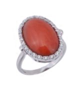 A coral and diamond ring, the oval cabochon coral (Corallium Rubrum) within a surround of brilliant