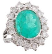 An emerald and diamond cluster ring, the oval shaped emerald in a semi collet setting, within a