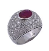 A ruby and diamond ring, the central oval shaped ruby in a collet setting, within a surround of