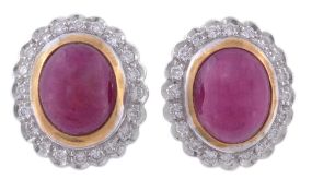 A pair of ruby and diamond ear clips, the central oval cabochon ruby in a collet setting, within a