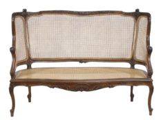 A Victorian walnut and caned bergere settee, late 19th/early 20th century, with a carved crest rail,
