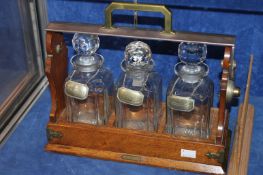 An oak tantalus with three glass decanters and associated plated labels for `Whiskey`, `Sherry` and