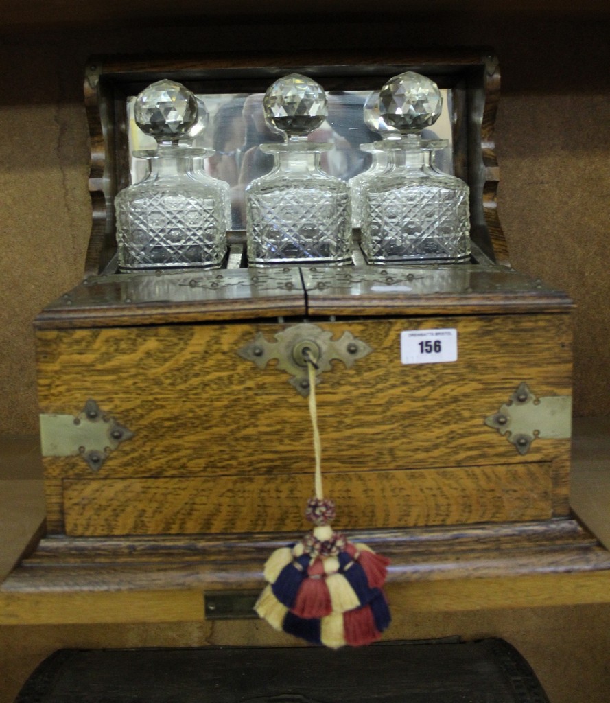 An early 20th century oak and EPNS mounted tantalus, containing three cut glass decanters and