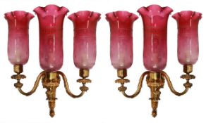 A pair of gilt bronze and cranberry glass fitted three light wall appliques, early 20th century, the