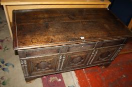 An antique Flemish oak coffer with a plank lid and triple panel front, carved with recessed