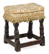 A Charles I oak covered stool, circa 1630, the fabric covered seat above a moulded frieze and