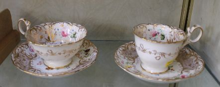 Two Ridgway style Rococo Revival cups and saucers painted with floral panels set inside gilt