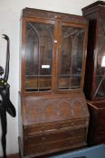 An early 20th Century oak bureau bookcase with arched astragal glazed doors enclosing shelves,