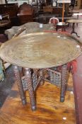 A Middle Eastern engraved brass tray top table 58cm high, 70cm diameter