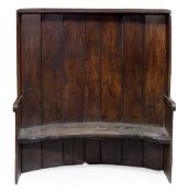 An oak tavern settle, late 18th/early 19th century, of concave form, the boarded tall back above a s