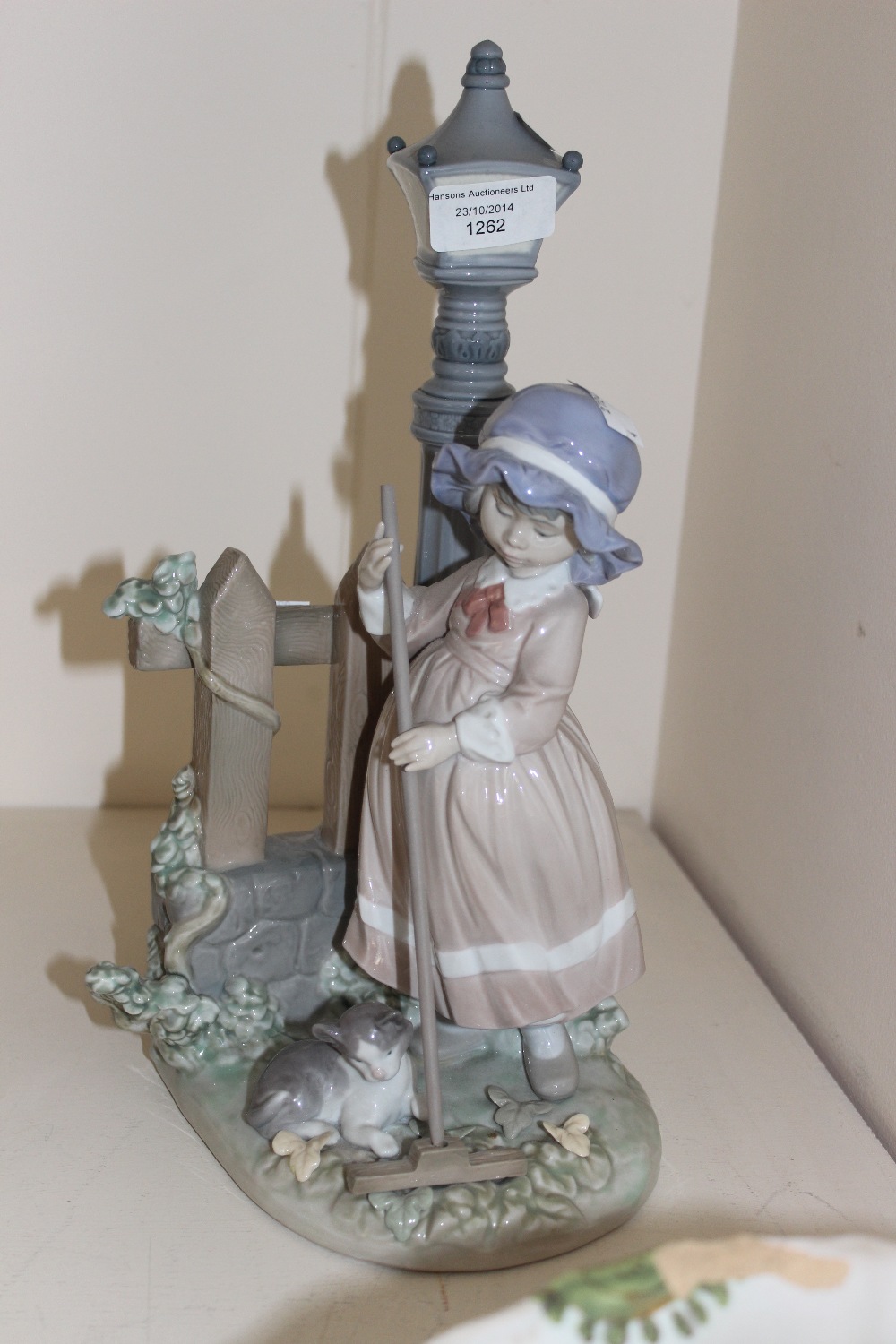 A Lladro girl sweeping beside a lamp post