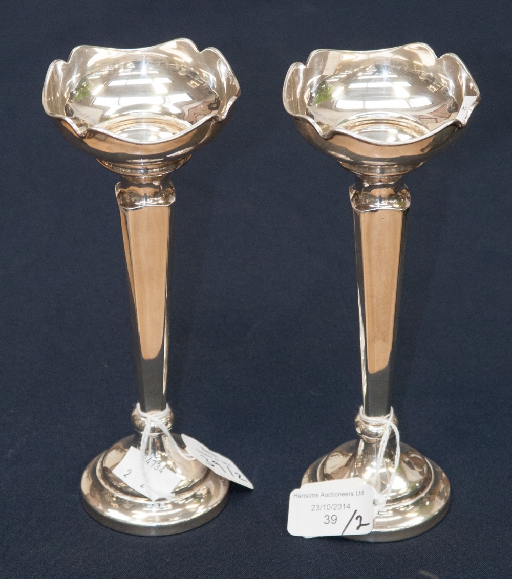 A pair of silver vases/candle holders with shaped flared rims on square section tapered stems,