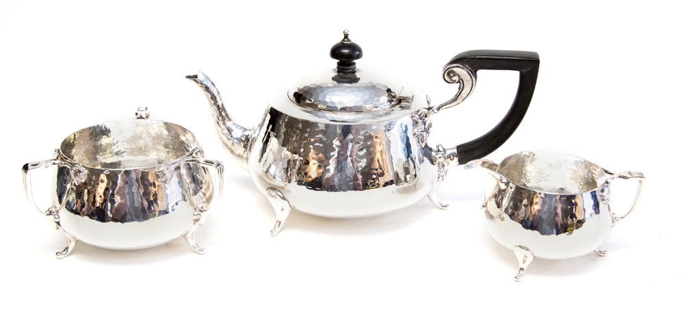 An Arts and Crafts silver three piece tea service, planished form with applied stylized tulip