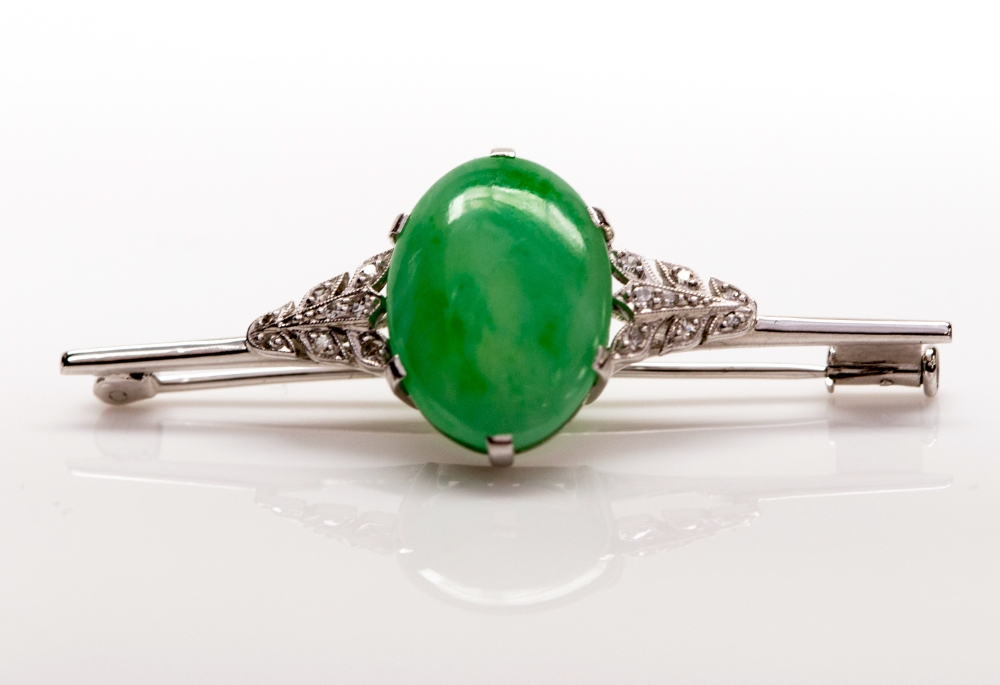 An Art Deco bar brooch measuring approx 5 cm long, set with a single oval jade cabachon flanked by