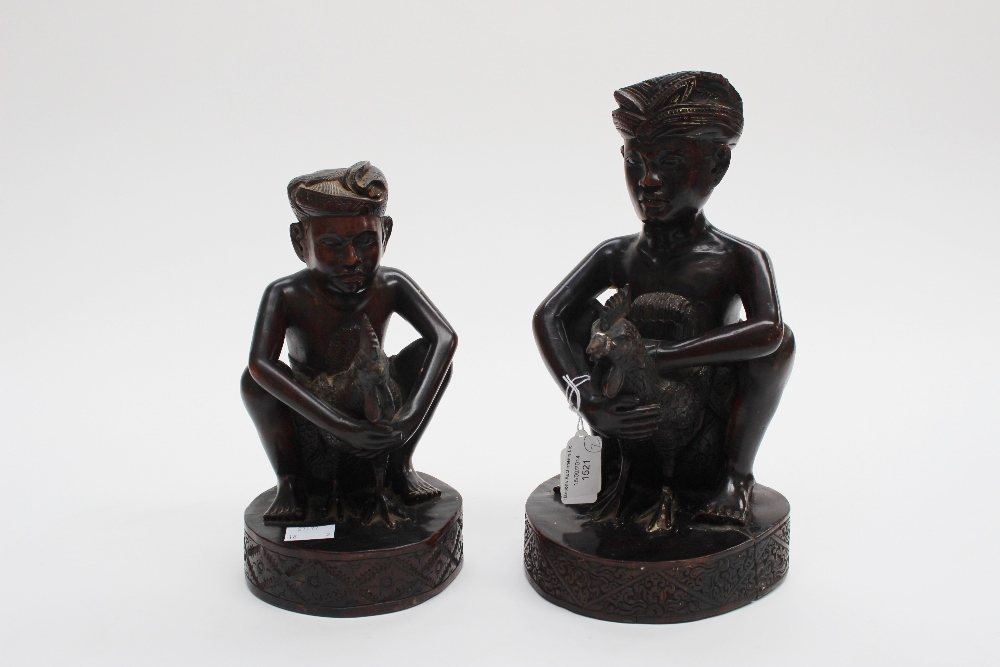 Two hardwood carved Indian figures, each of a seated man wearing head scarf and holding a cockerel
