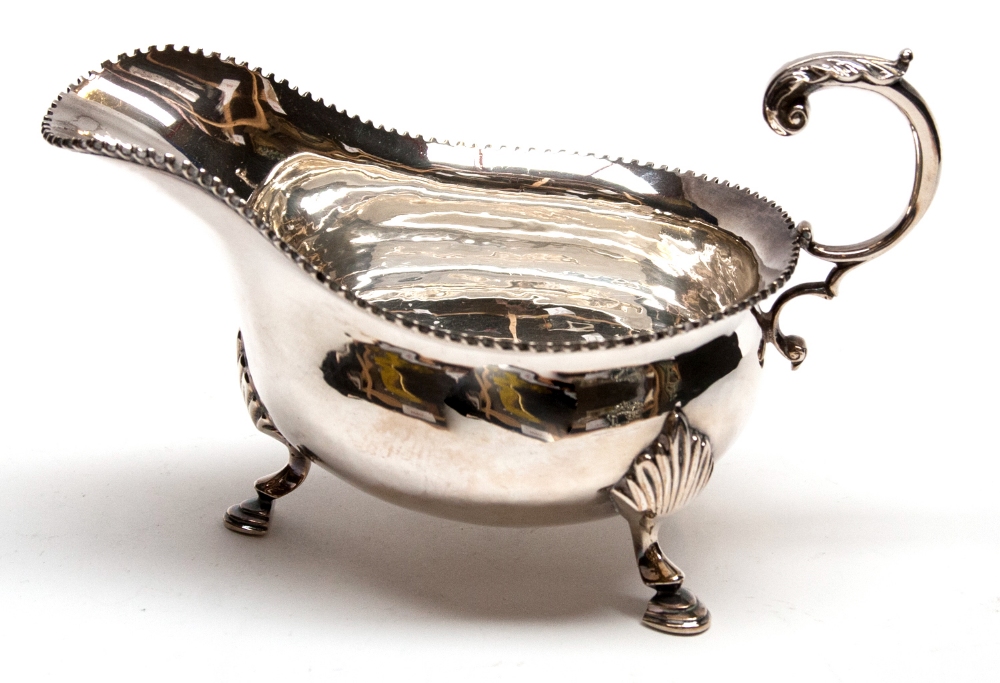 A modern silver sauce boat of George II style with toothed border and open scroll handle, on three