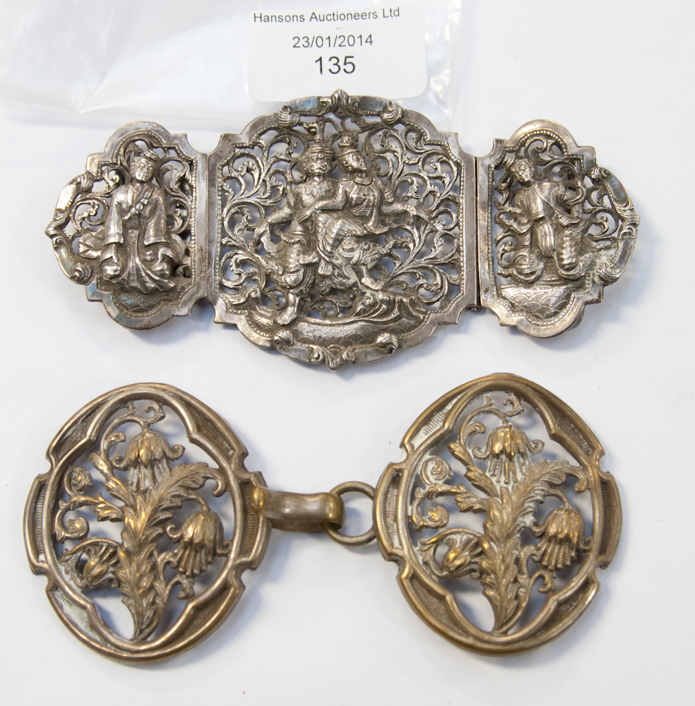 An Indian white metal buckle with Hindu figures and a brass buckle (2).
