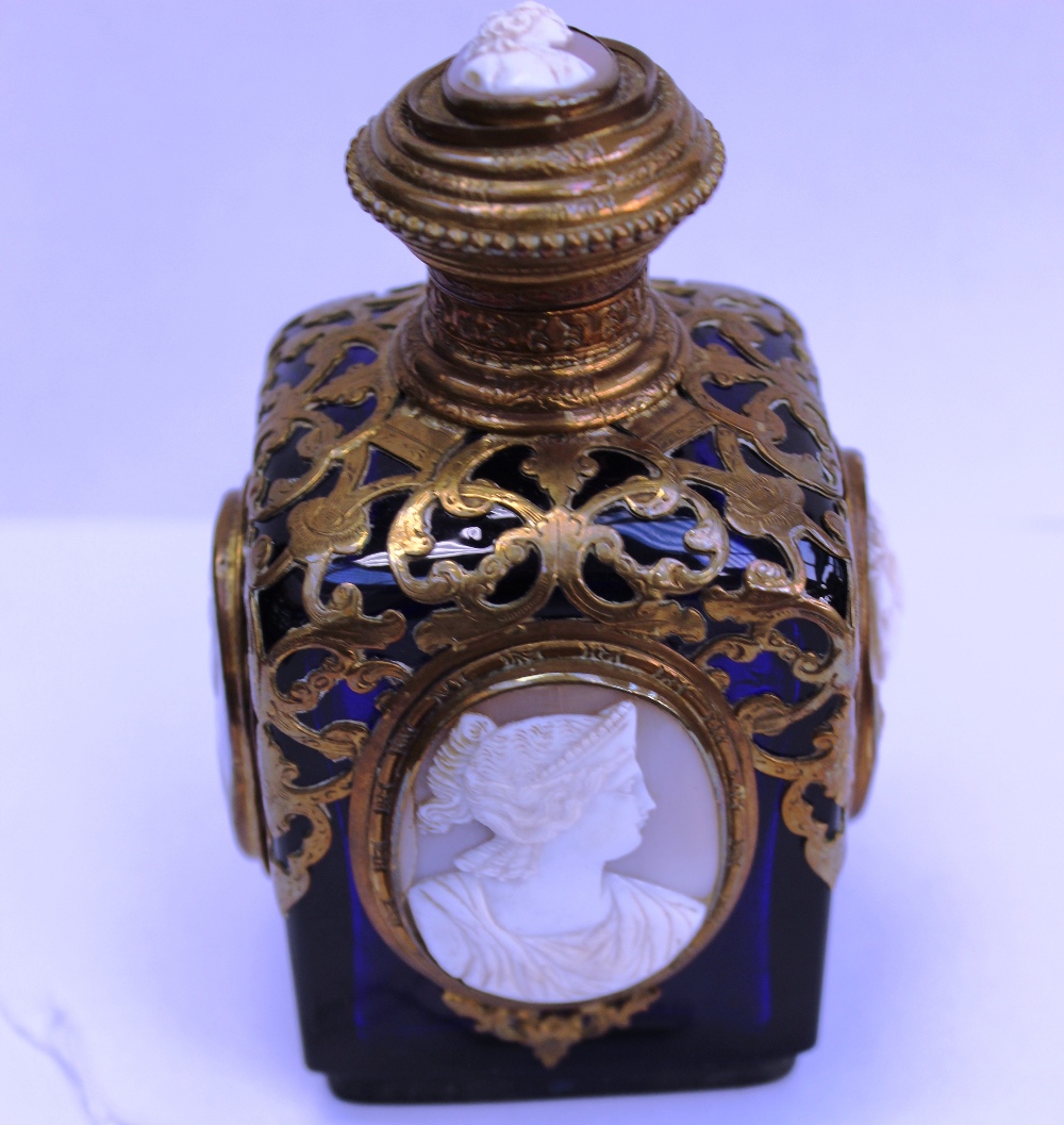 A dark blue glass perfume bottle, overlaid with gilt metal, each side panel is decorated with framed
