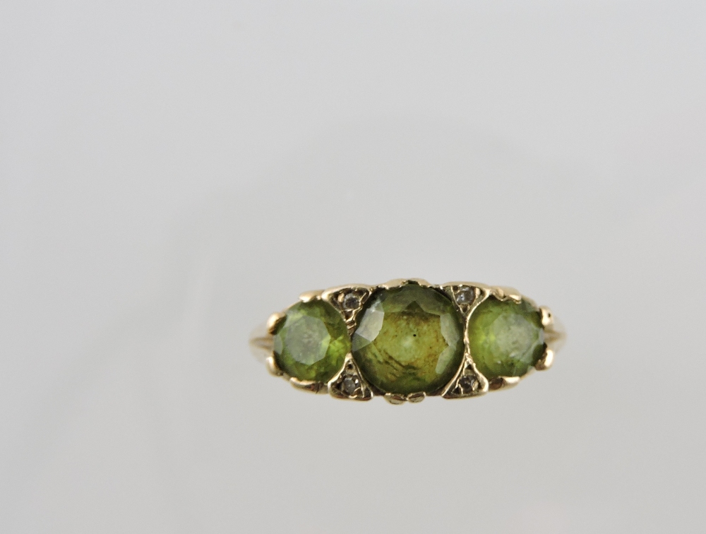 A 9ct ring set with three peridot and four small diamonds on a raised scroll mount.