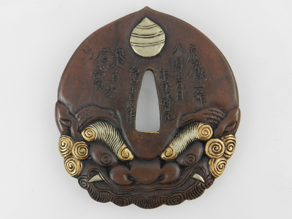 A Japanese cast patinated bronze Katana Tsuba, stylised as a Shi Shi mask, bears script to verso.