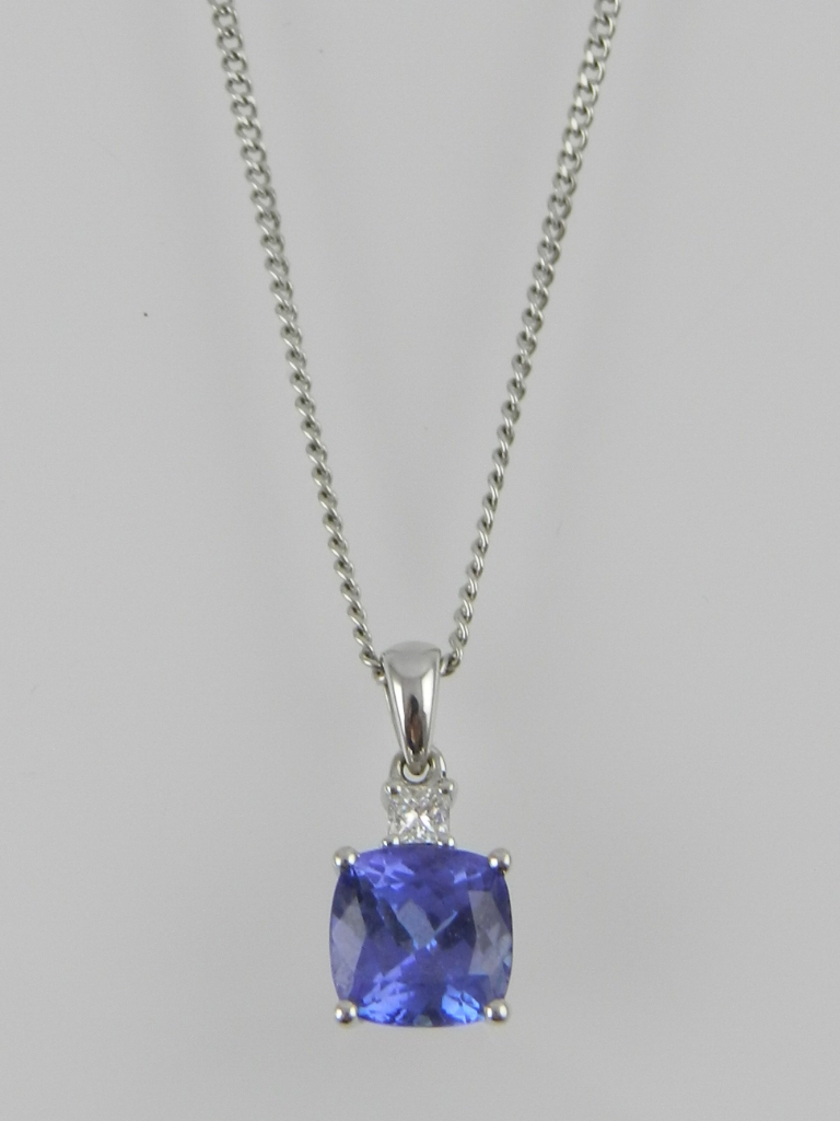 An unusual white metal tanzanite and diamond pendant, set with a round cut diamond above a cushion