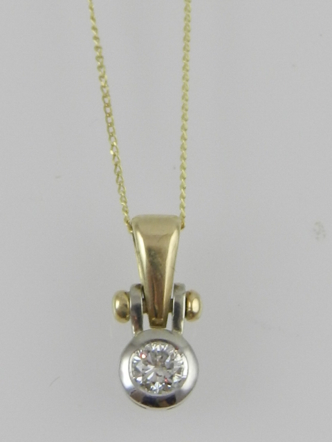 A yellow and white metal diamond collet set pendant and fine link chain, the mount stamped 10k.